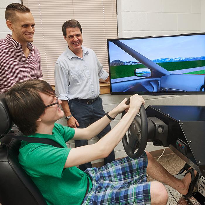Psychology student takes a spin in the Driving Simulator as a graduate student and Professor record the results.
